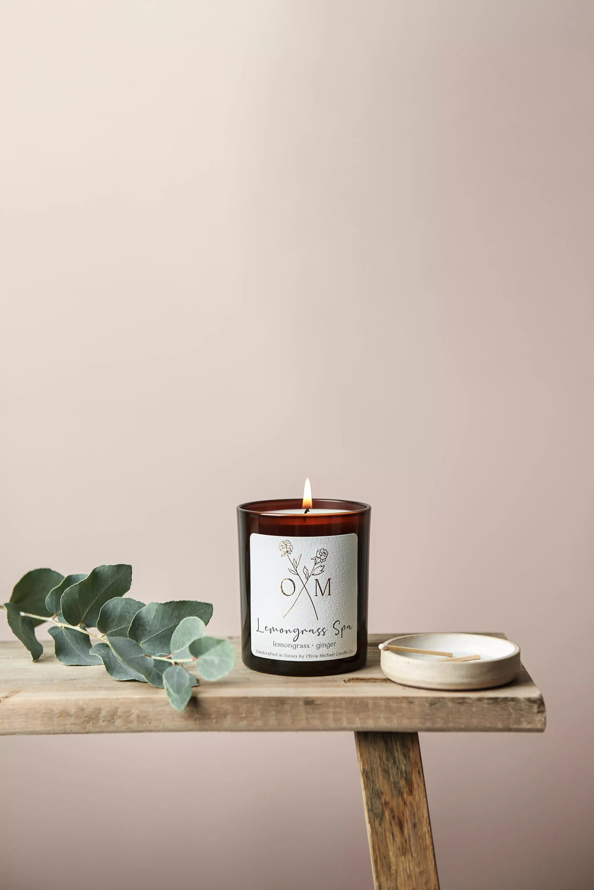 Our Lemongrass Spa scented candle is lit and on display in an amber glass jar.