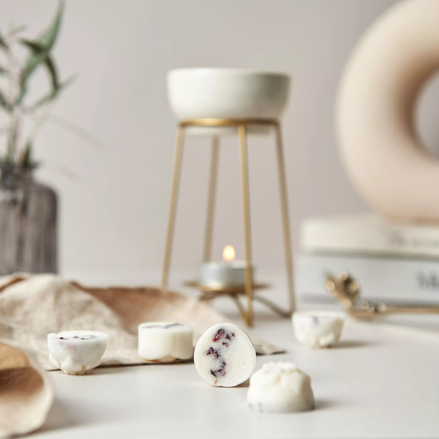 Our Cedarwood and Jasmine Wax Melts are loosely scattered with a bronze wax warmer and a tea light in the background.