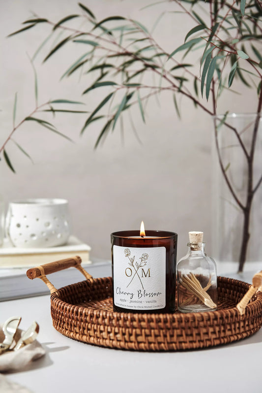 Our Cherry Blossom scented candle is lit and on display in an amber glass jar.