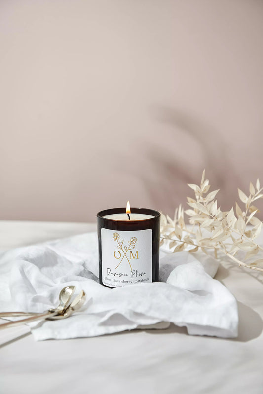 Our plum and black cherry scented candle is lit and on display in an amber glass jar.