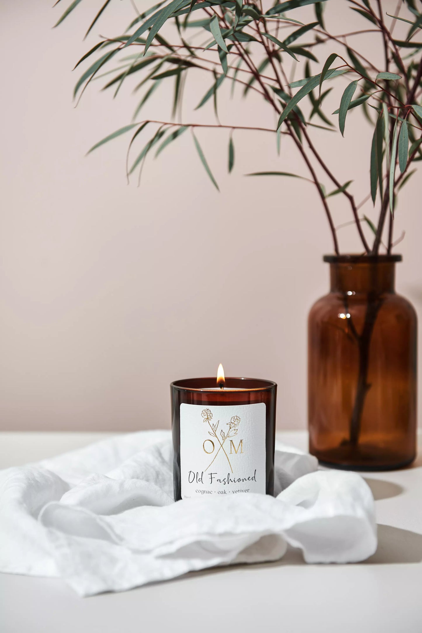 Our cognac and oak scented candle is lit and on display in an amber glass jar.