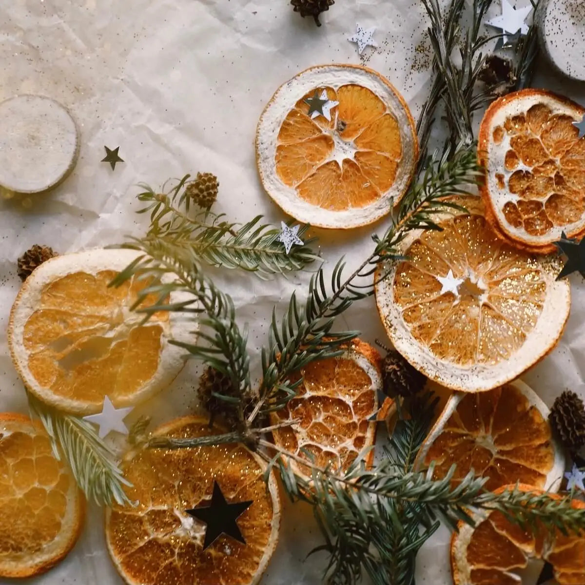 A flatlay of slices of orange, glittery stars and pine tree branches