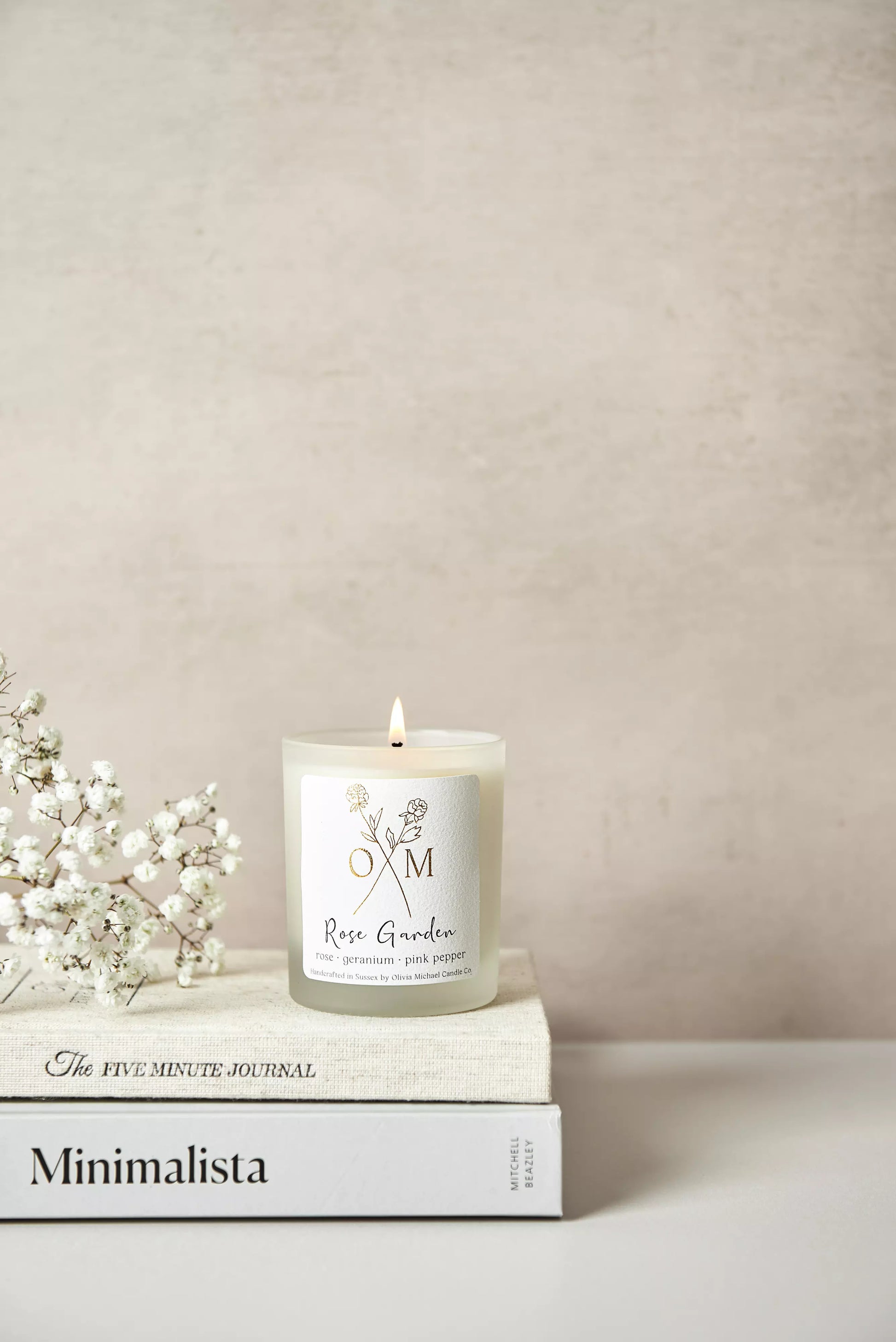 Our rose aromatherapy candle is lit and on display in a clear frosted glass jar.