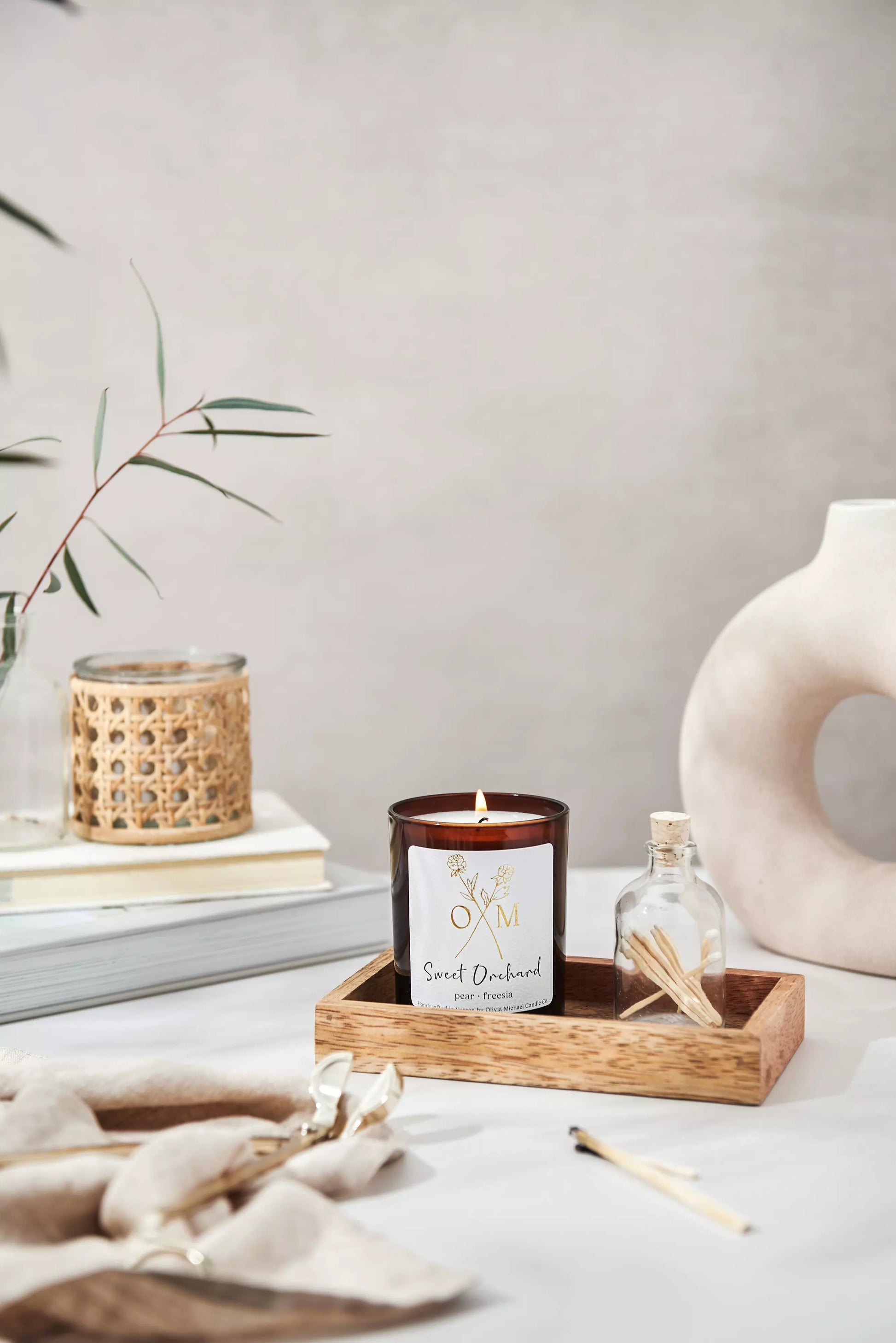 Our Sweet Orchard scented candle is lit and on display in an amber glass jar.