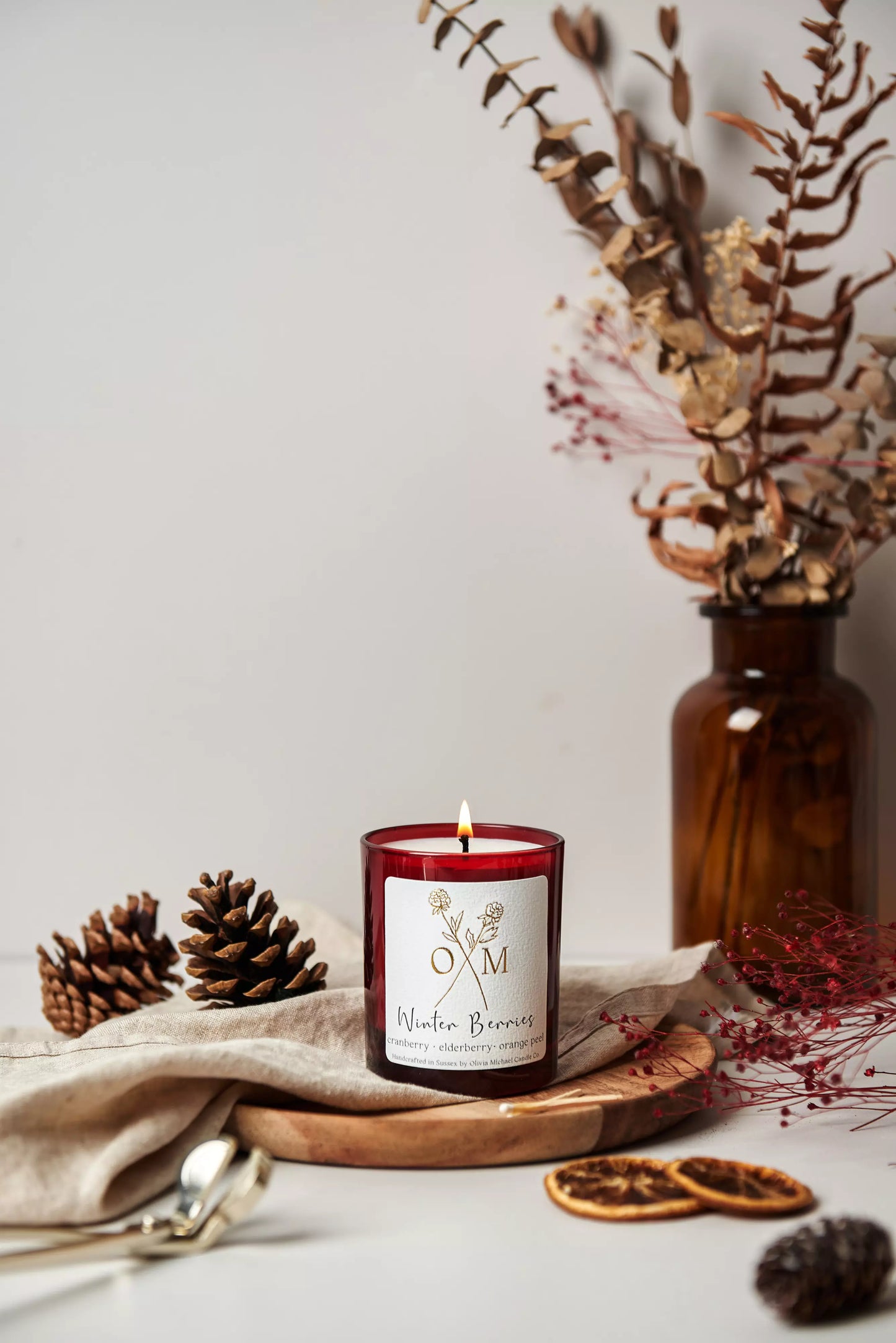 Our cranberry and elderberry scented candle is lit and on display in an amber glass jar.