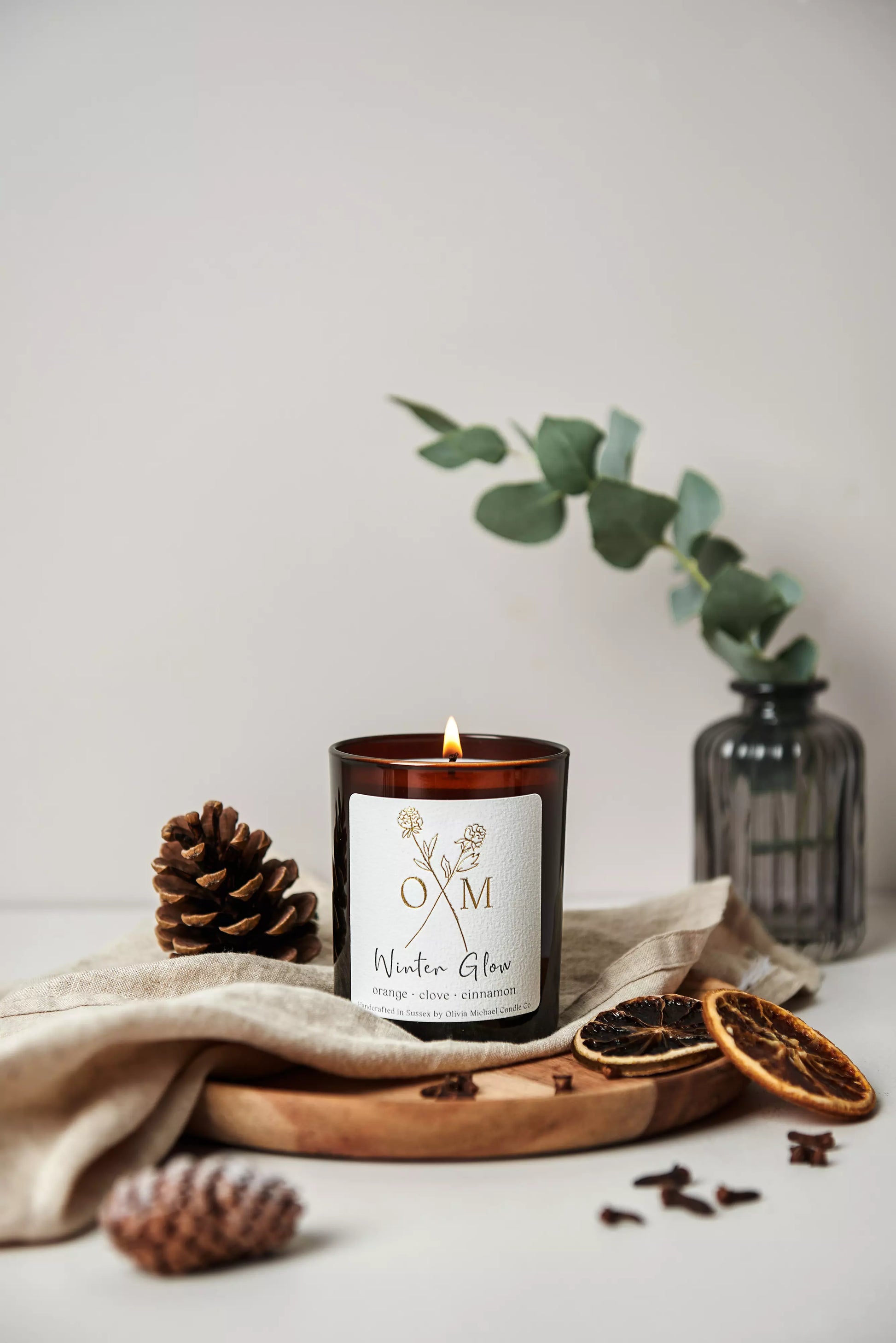 Our orange and clove scented candle is lit and on display in an amber glass jar.